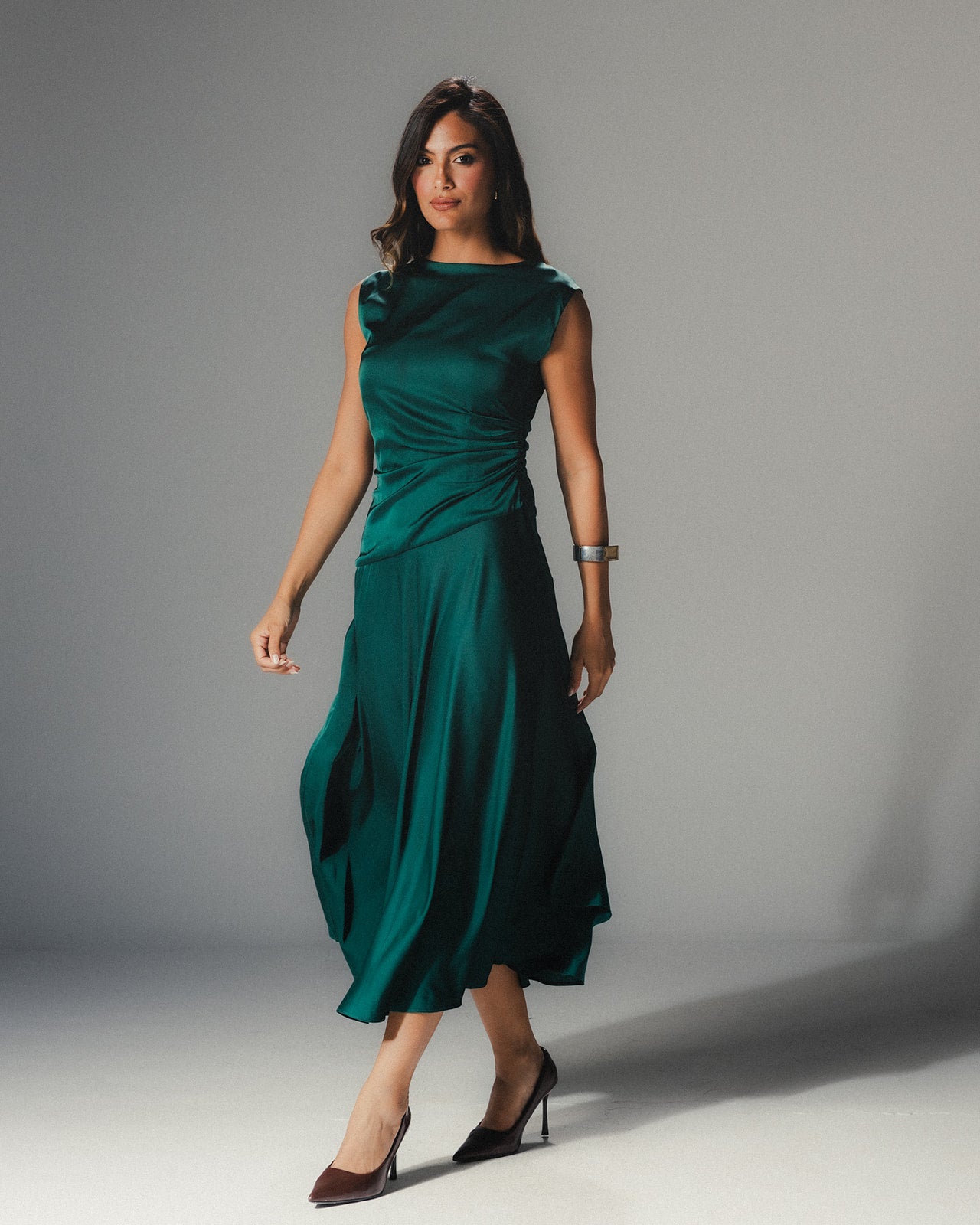 Model walking in the MYSHA emerald green satin dress, highlighting the modern asymmetrical hem and fluid movement