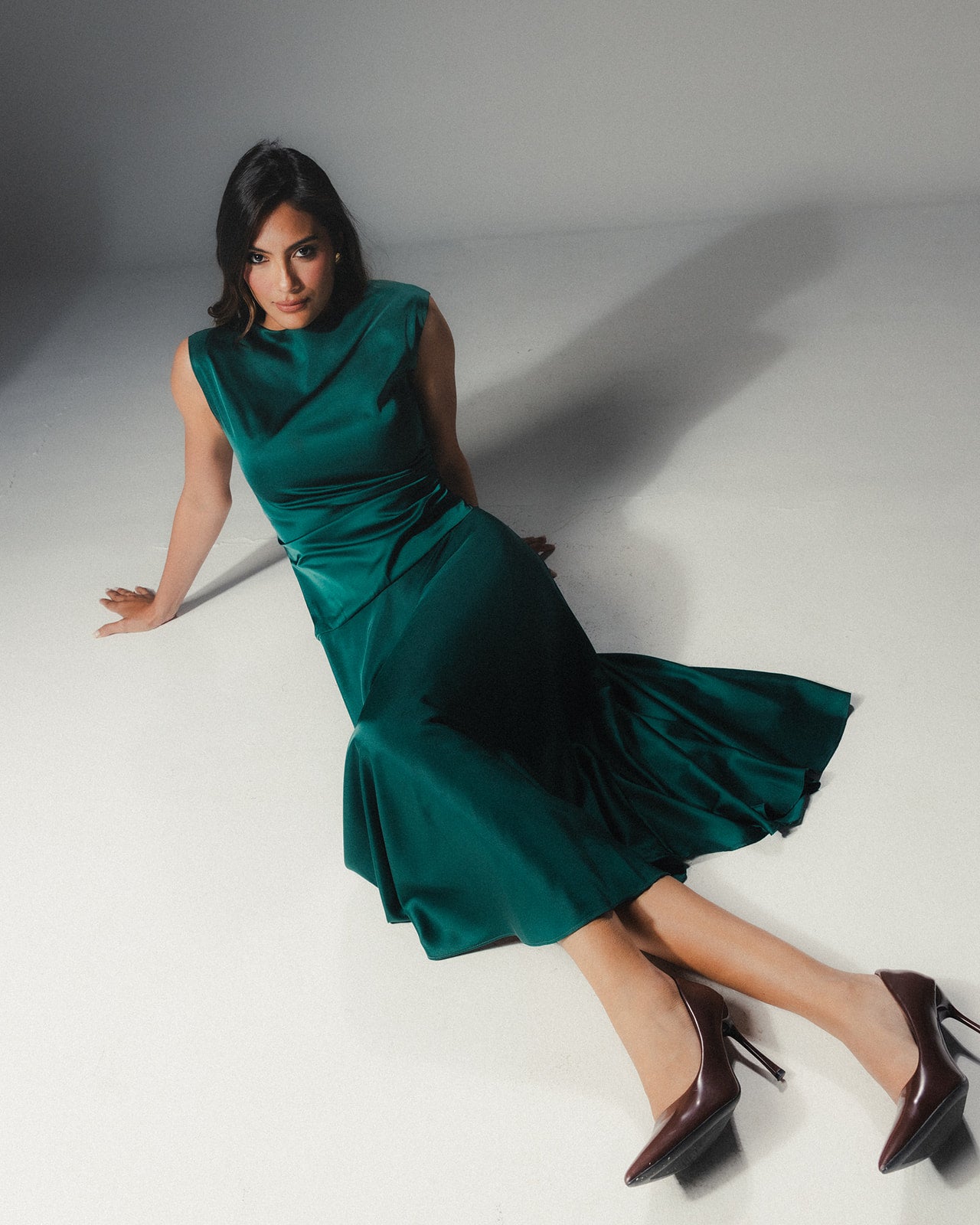 odel reclining in the MYSHA emerald green Satin Armani midi dress showing the fluid drape and high-shine finish