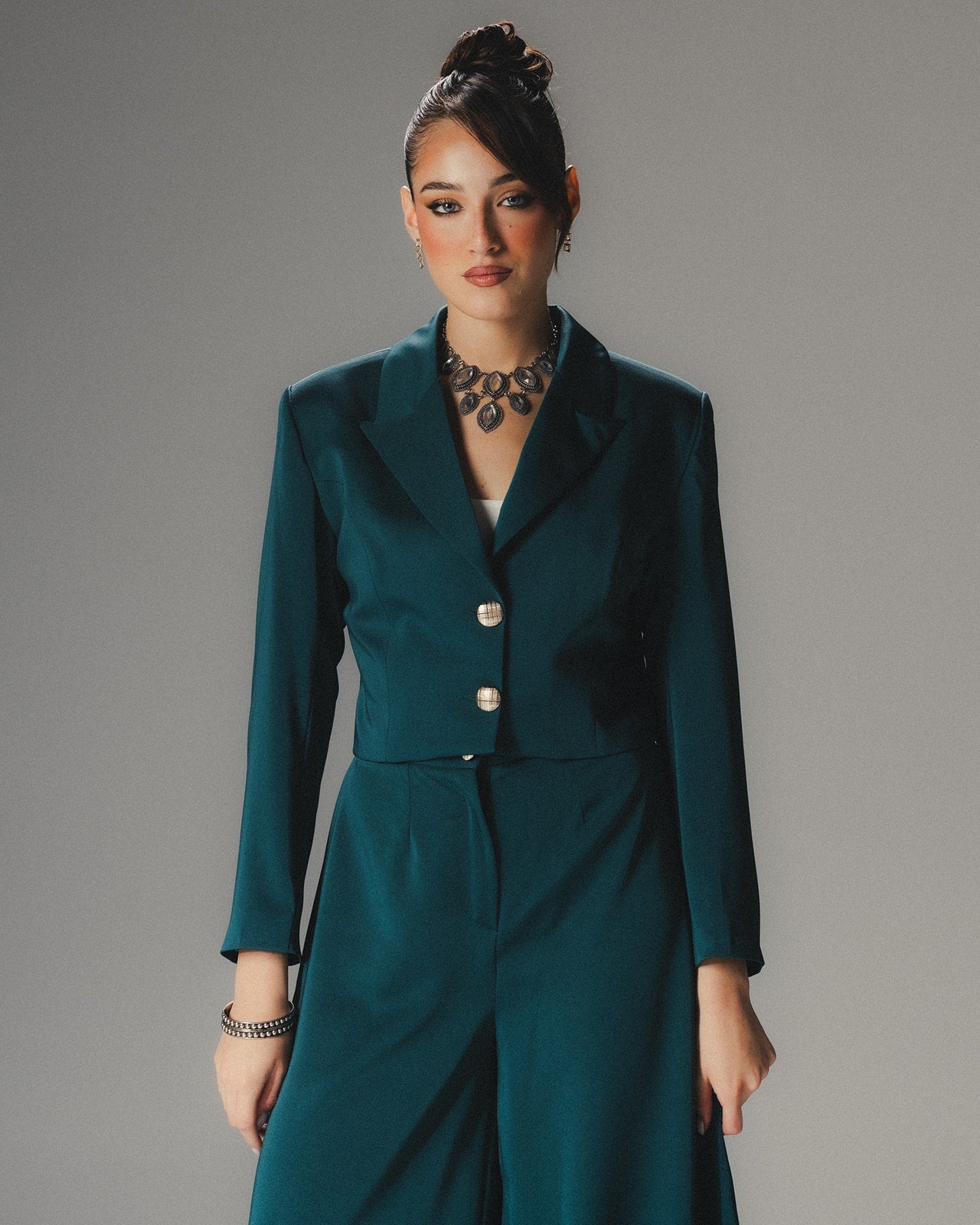 Front view of MYSHA Emerald green cropped blazer in luminous satin crepe featuring sharp lapels and silver-toned statement buttons.