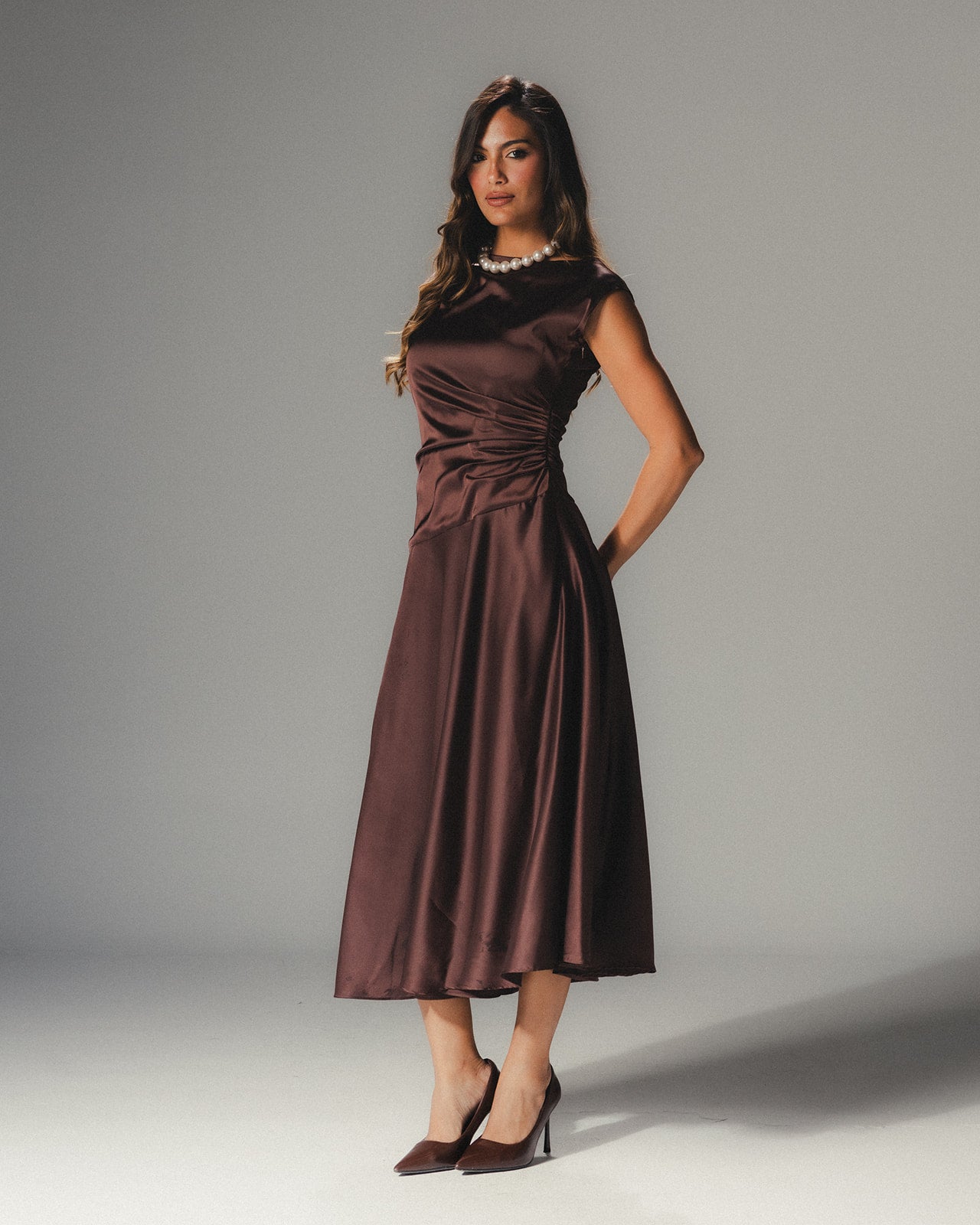 Model wearing the MYSHA Espresso brown Satin Armani midi dress featuring a high-neck and architectural drape.