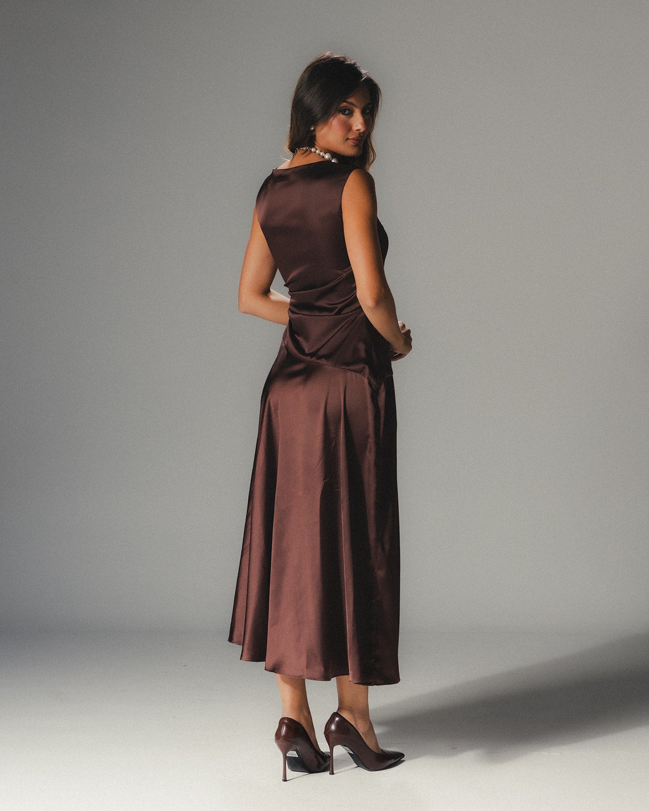 Model wearing the MYSHA Espresso brown Satin Armani midi dress featuring a high-neck and architectural drape.